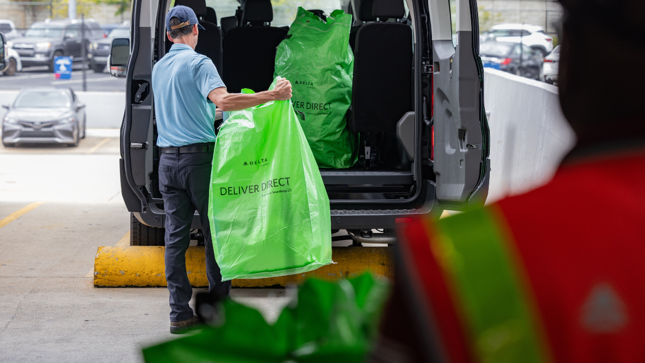 A delivery driver loads Delta Cargo DeliverDirect branded bags into a van for last-mile delivery